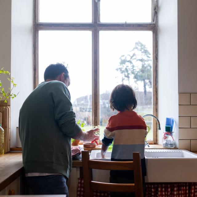 Father and child standing in kitchen together washing up.