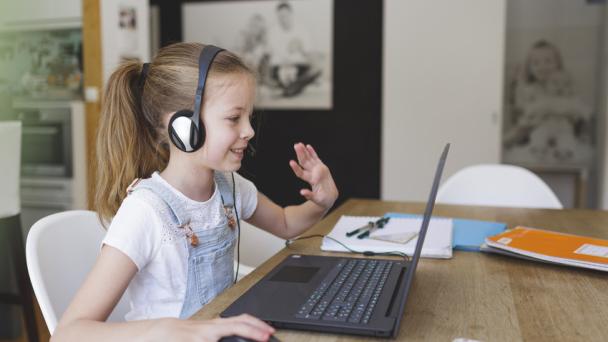 A young girl sitting at a laptop, learning online.