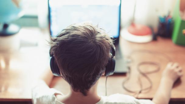 Child of about 10-13 years old sitting at a computer with headphones on. 